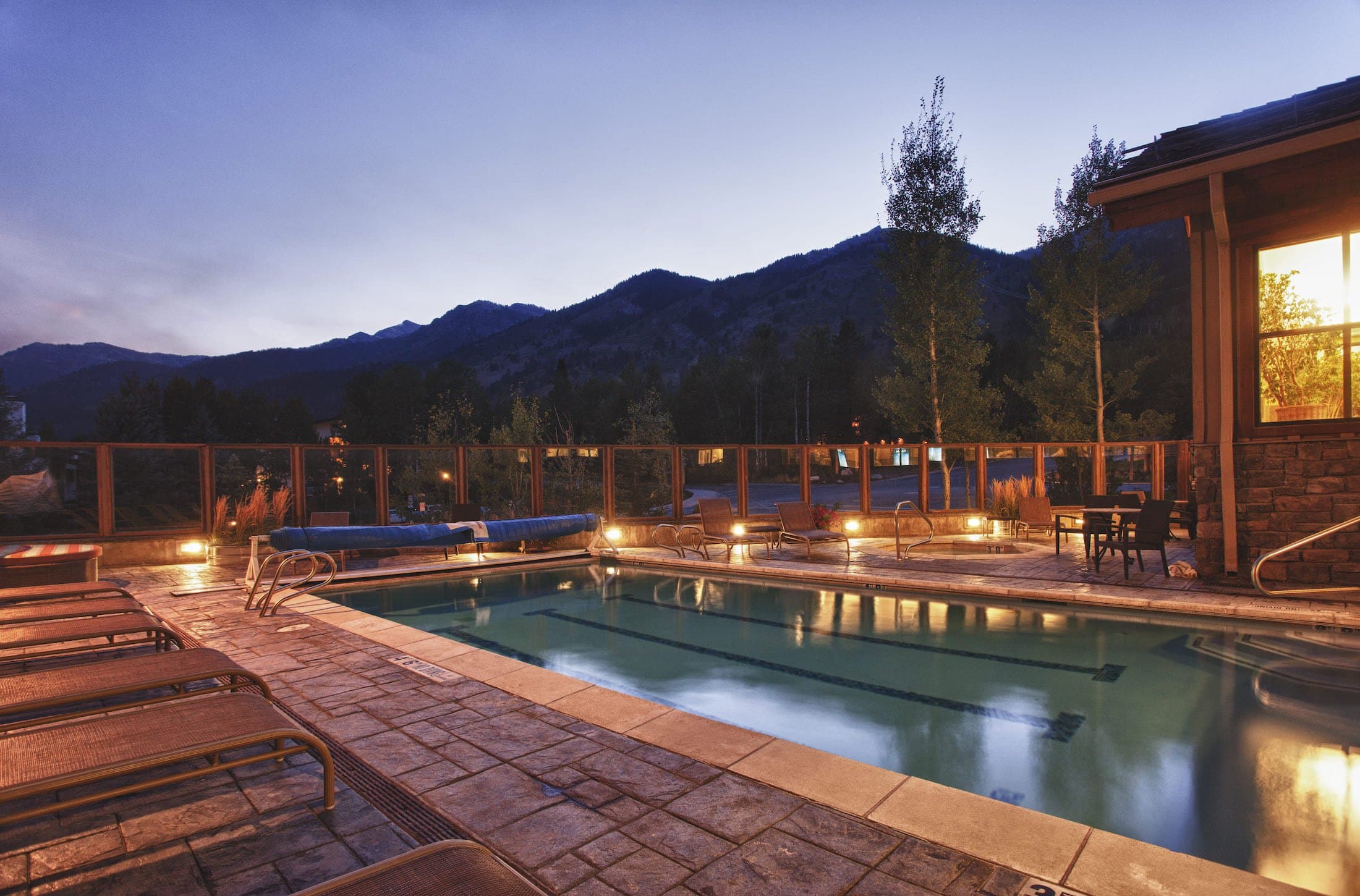 An outdoor pool at Teton Mountain Lodge with a hot tub and plenty or relaxing seating areas with the mountains in the background