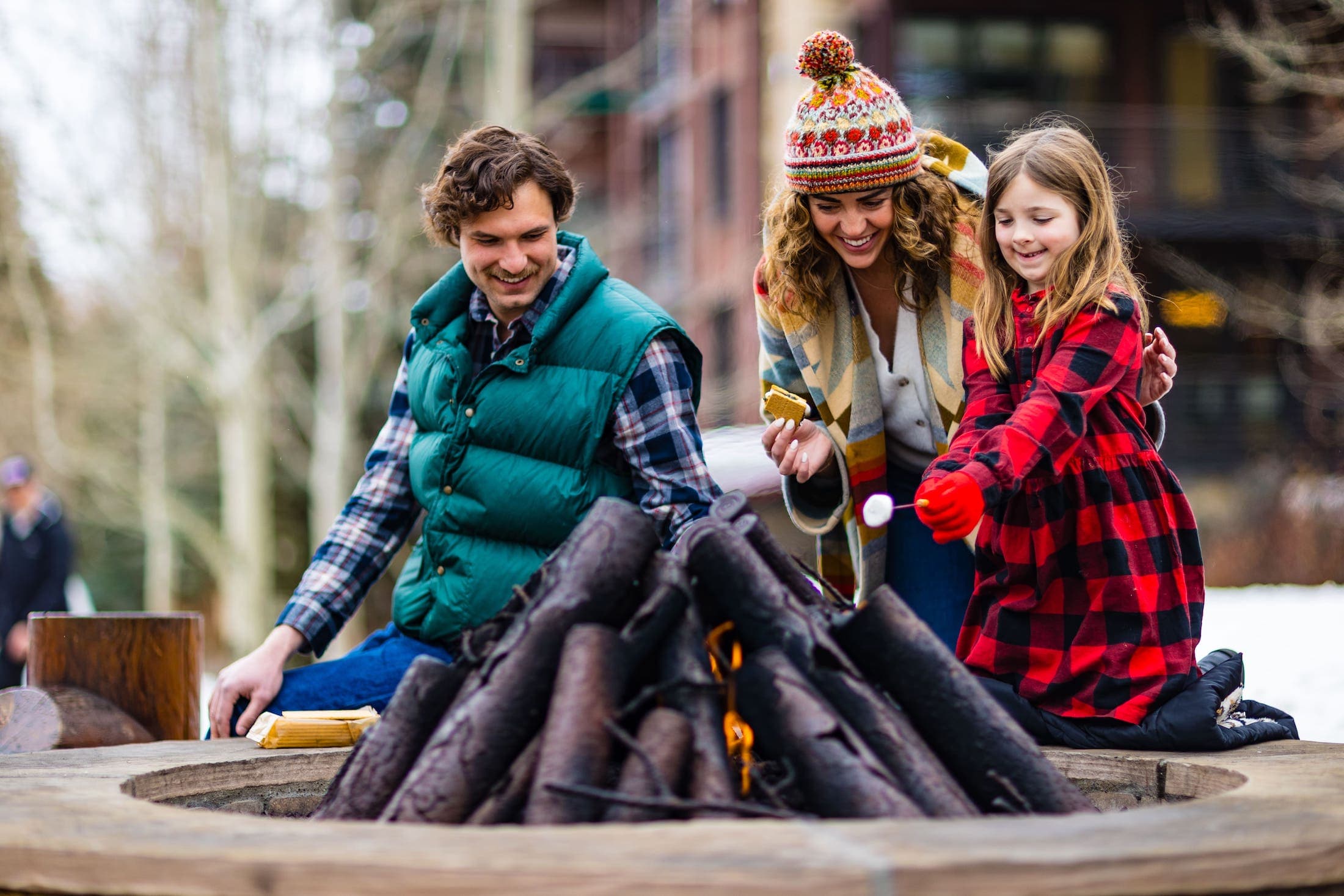 A family roasting marshmallows over a contained fire pit during the day