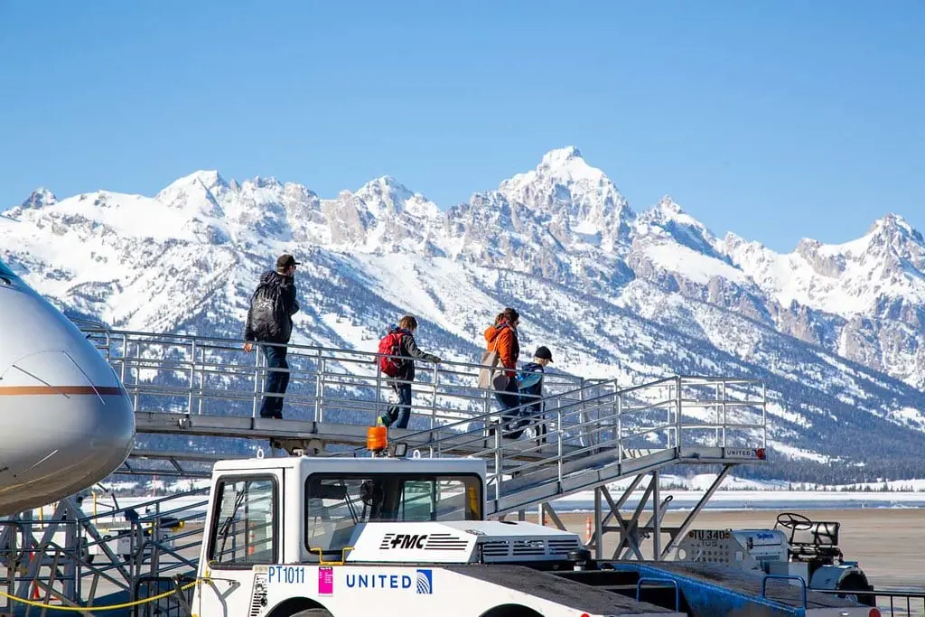 A family exiting off of an airplane on the tarmac with snowy mountains in the background
