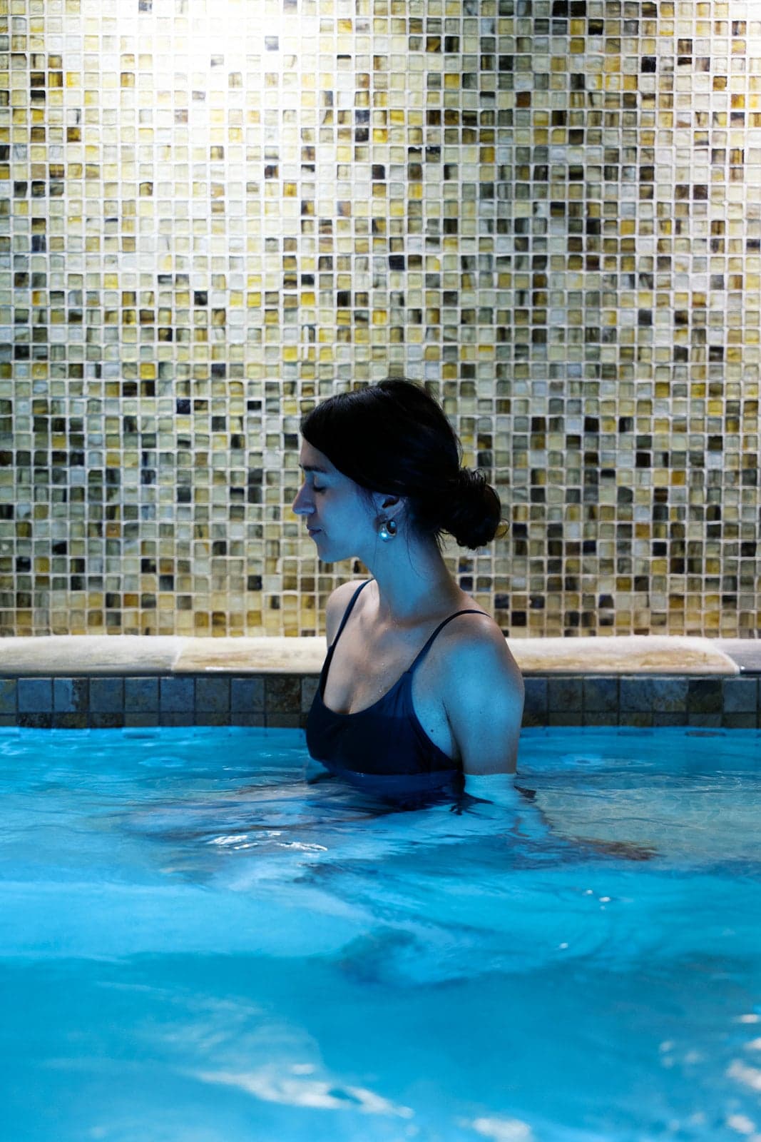 A woman sits in an indoor spa pool with lit blue water