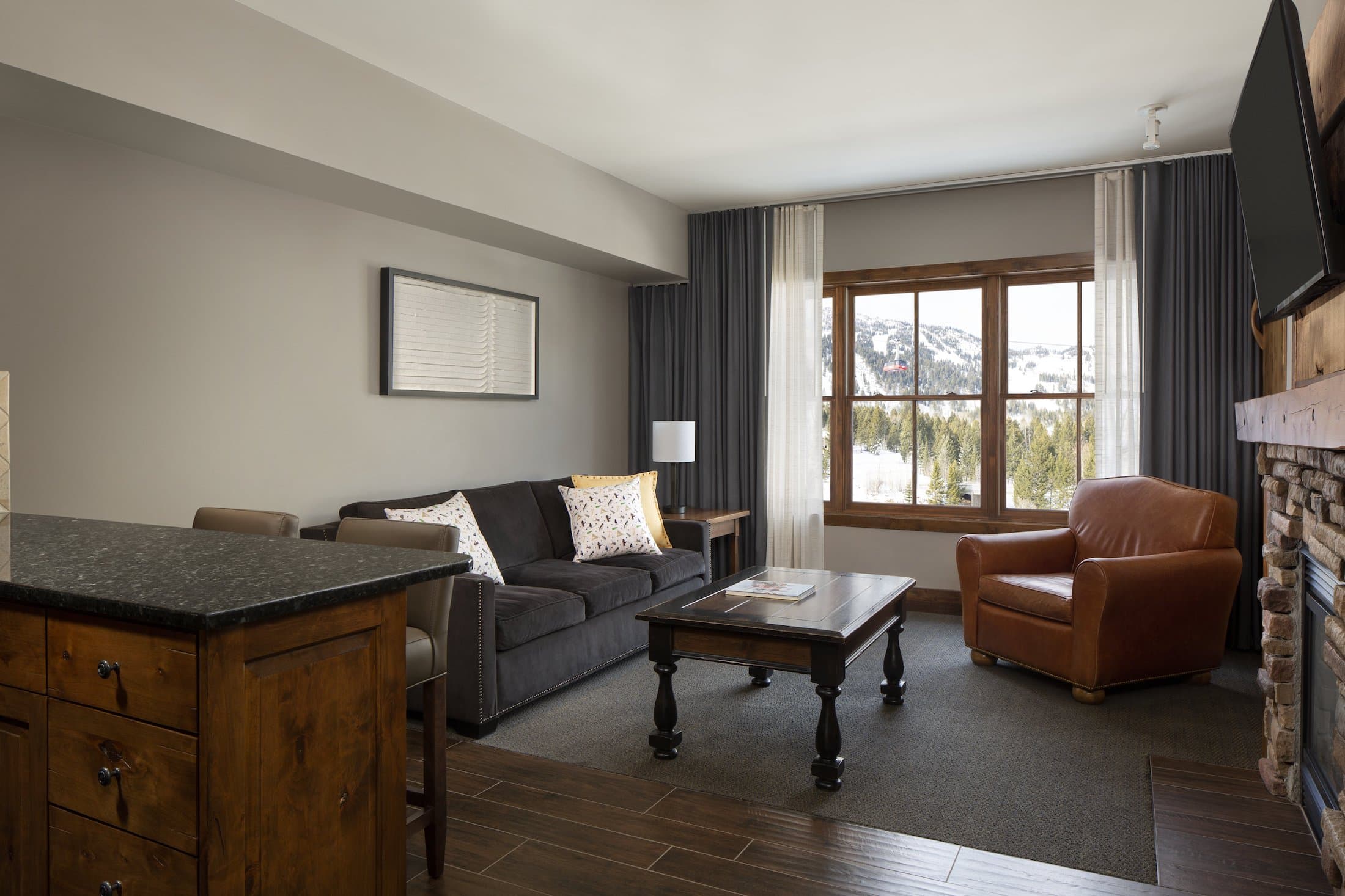 The living space with a fireplace, couch, chair, and kitchen island in the Teton Mountain Lodge Alpine Studio