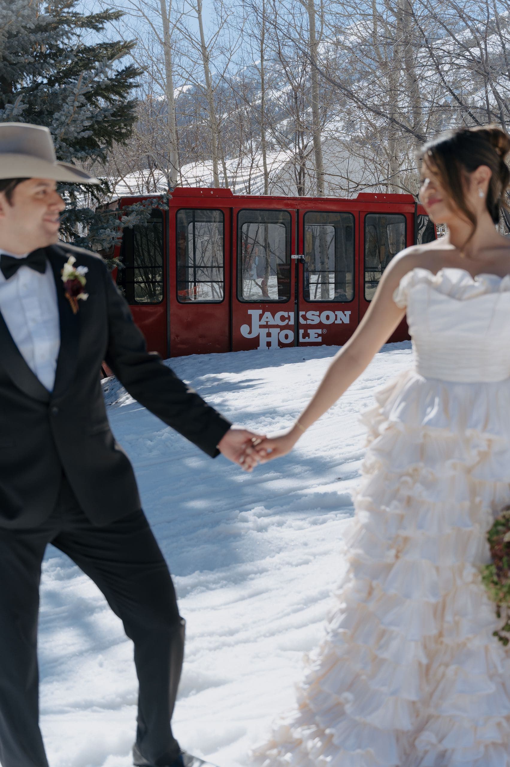 A photo of a wedded couple holding hands outside at front of an aerial tram, with the tram in focus while the couple is out of focus
