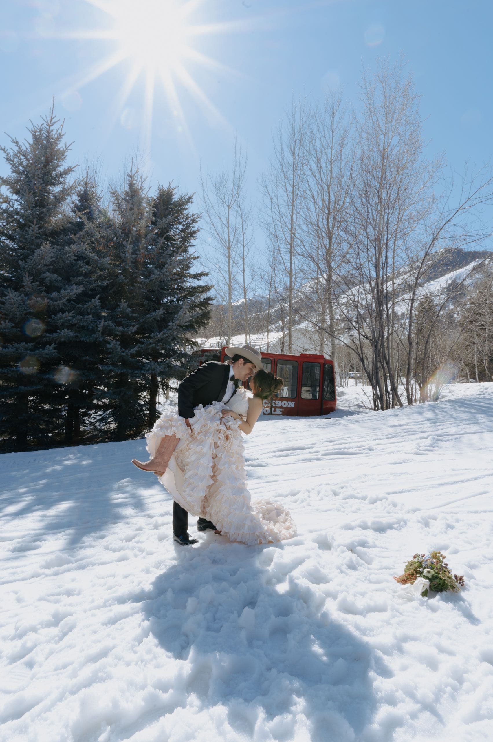 A photo of a wedded couple kissing outside in the snow, the man is wearing a light-coloured cowboy hat