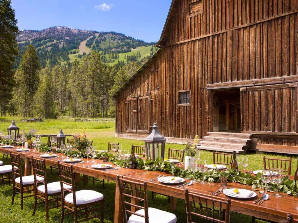 A photo of a rustic barn with a long outdoor table, with place settings in midday