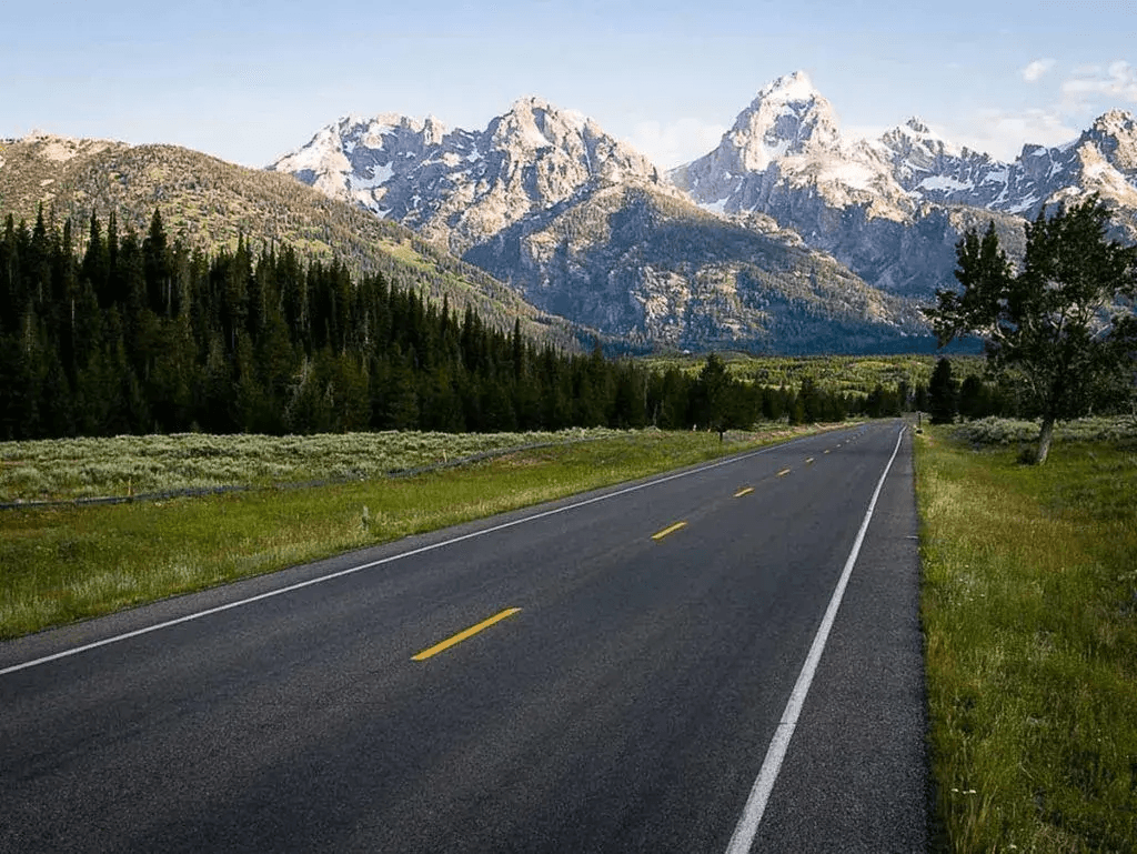 A photo of a two-lane uncontrolled access highway backdropped by the Tetons in the distance