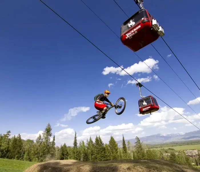 A person performs a trick on a mountain bike amidst the backdrop of a blue sky and a pair of aerial trams