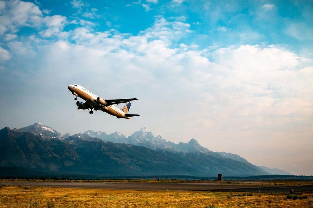 A United Airlines plane flies against a partially cloudy sky amid the backdrop of the Tetons