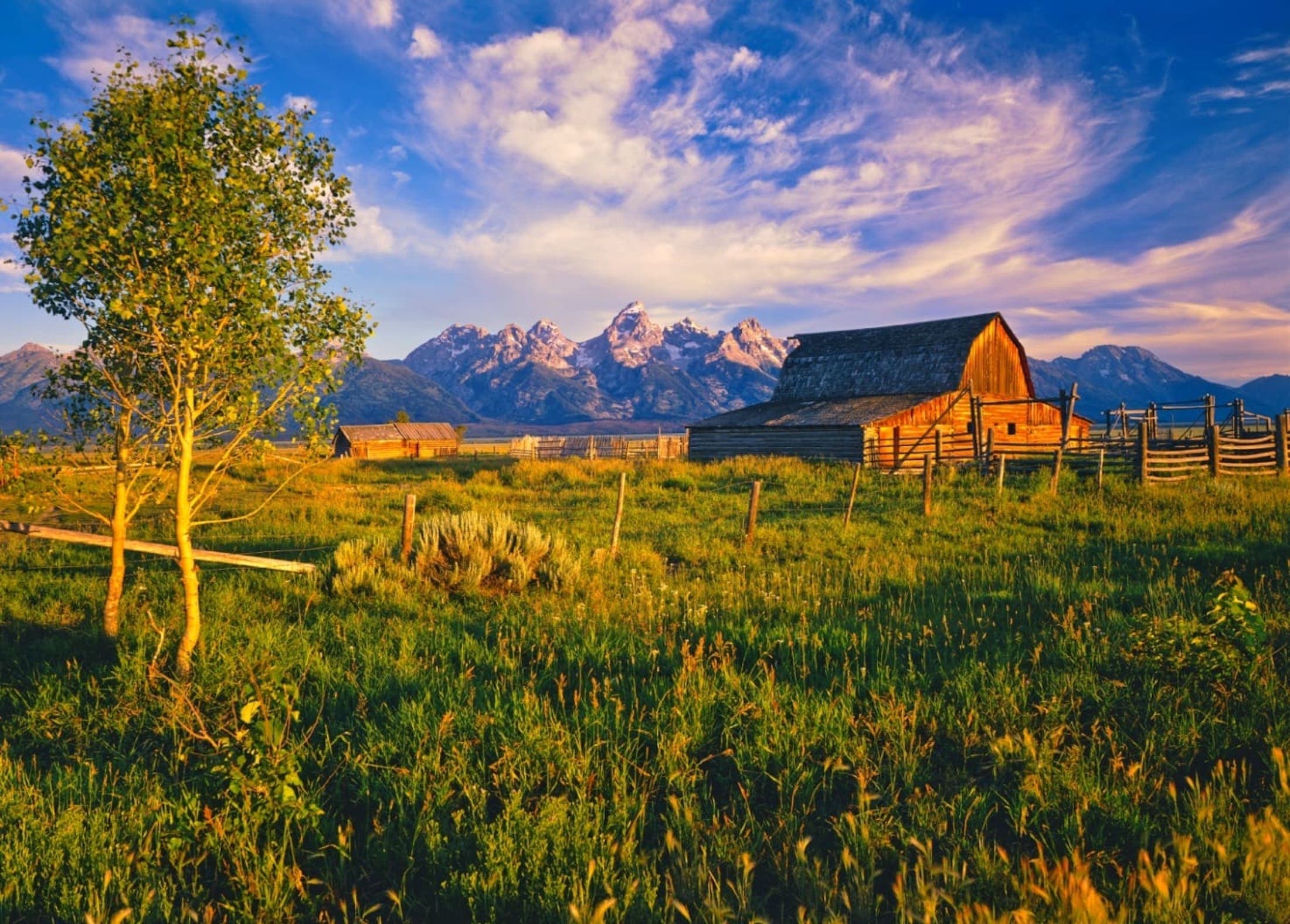 A photo of a rustic barn with the Tetons in the background during the golden hour