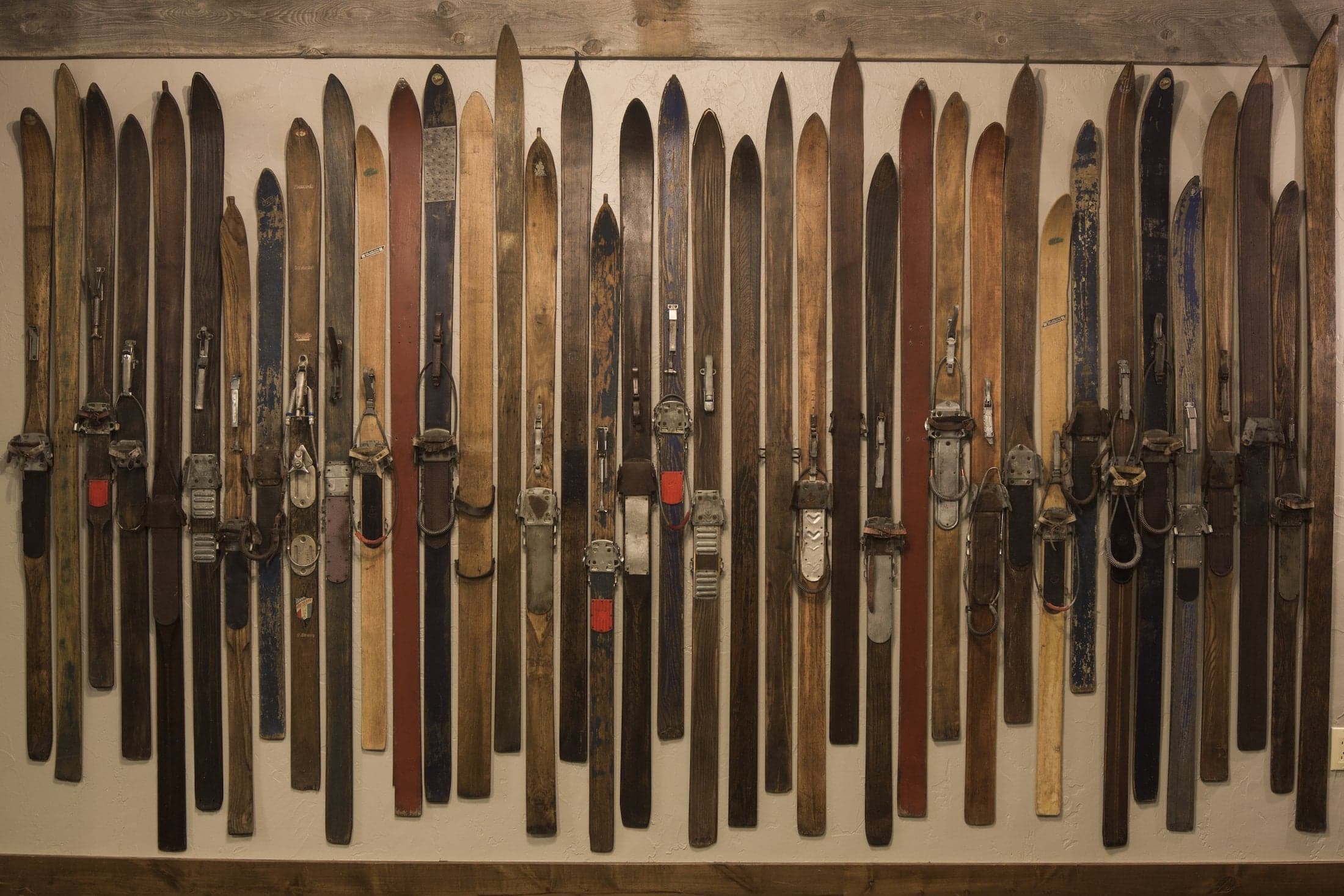 A photo of thirty-nine vintage individual skis of different colours and lengths mounted on a wall