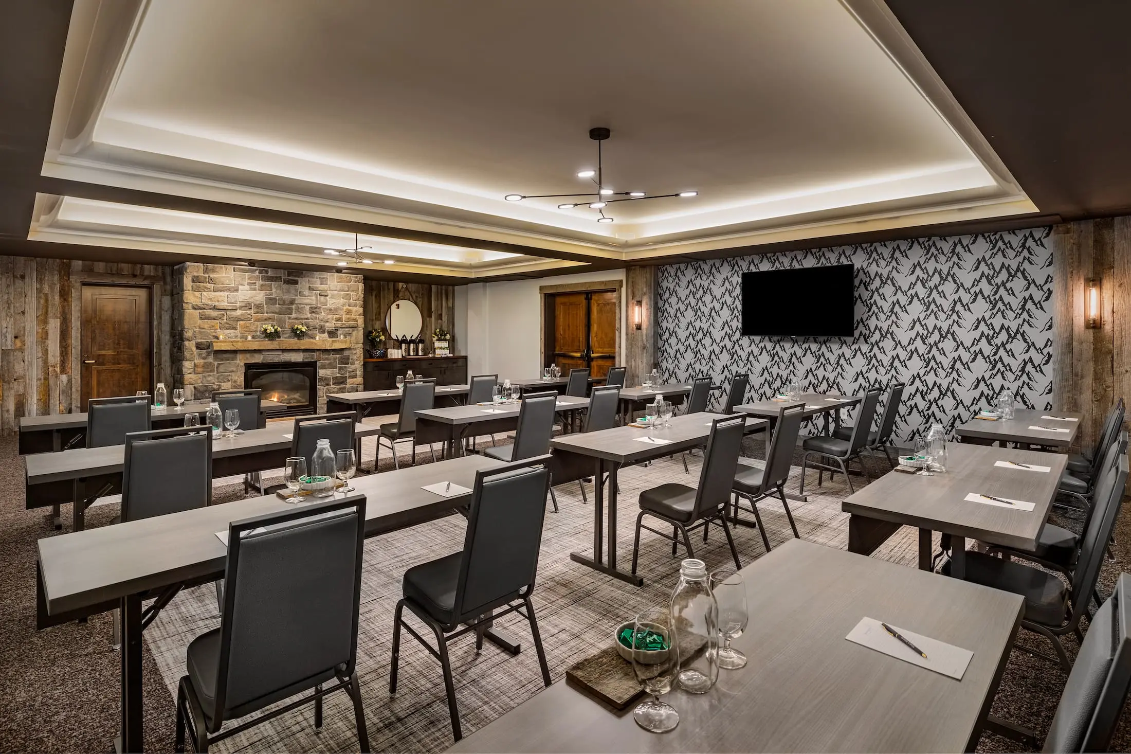 The Teton Room at Teton Mountain Lodge And Spa, 12 long desks with a paper pads and pens, water glasses, jugs, and bowls of mints, and two chairs each can be seen facing the front of the room