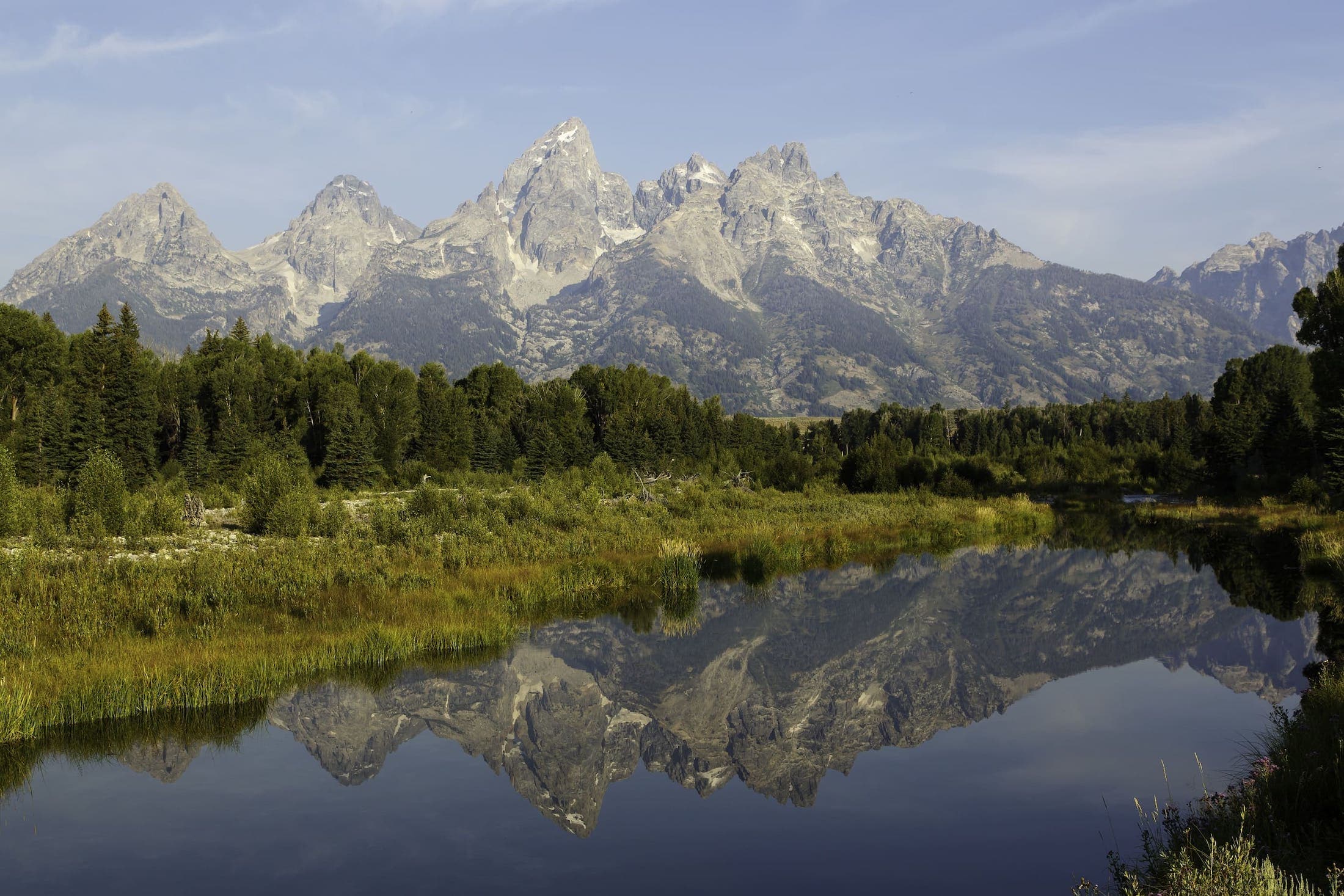 A photo of the Tetons with a lake and forest at front
