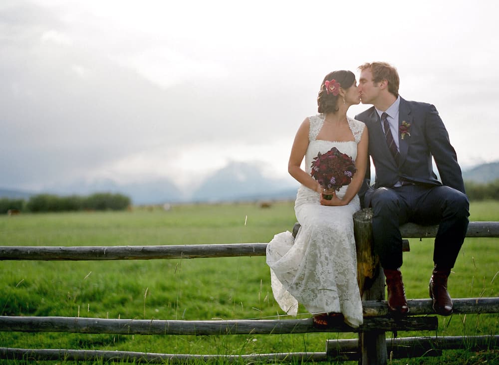 A wedding couple sitting on a rural timber fence