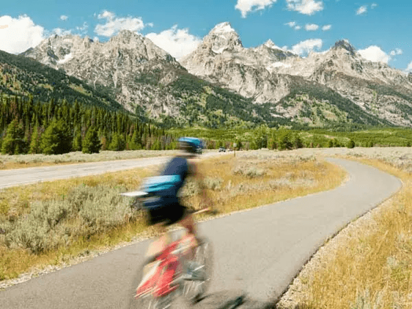A person riding a bike down a pathway in a field amidst the backdrop of a mountain range