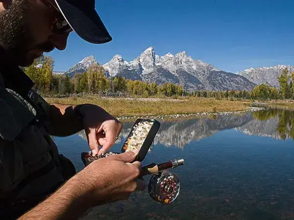 A man choosing a lure to use for fly fishing, against the backdrop of a mountain range and a lake