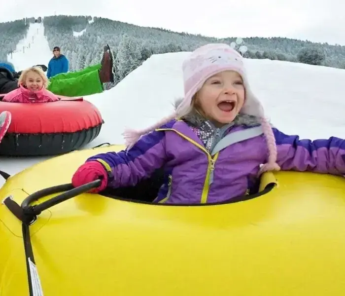 A group of children slide down a hill in snow tubes